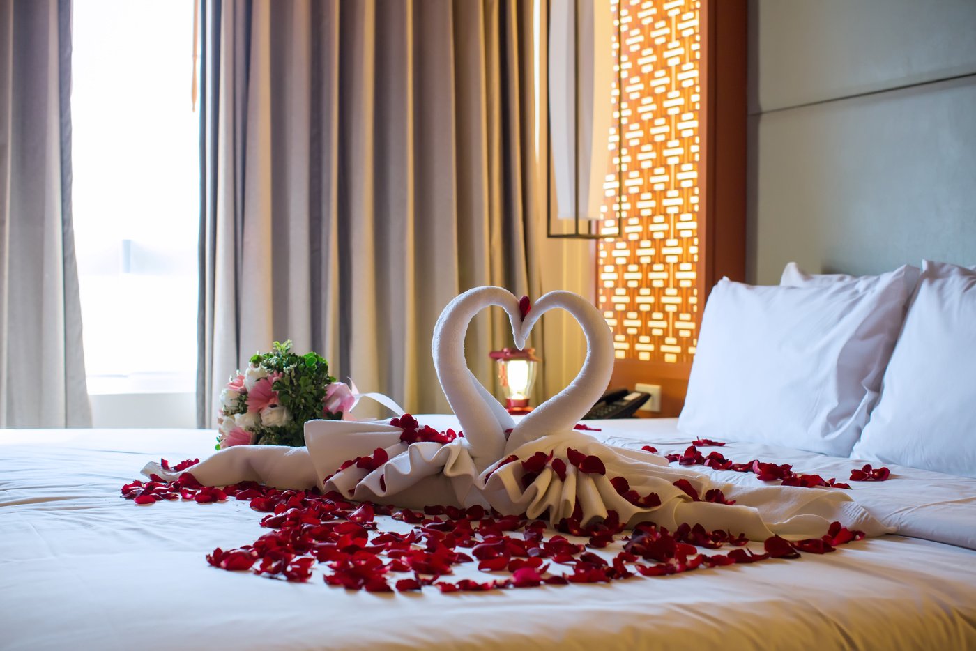 two swans made from towels are kissing on honeymoon white bed.